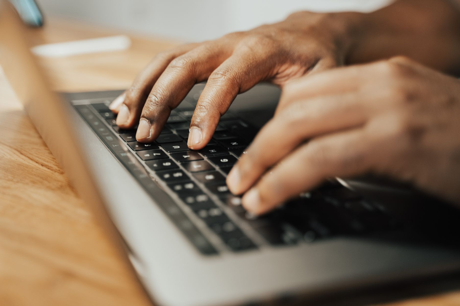 Skupione dłonie piszące na klawiaturze laptopa na drewnianym stole — praca zdalna wieczorową porą.